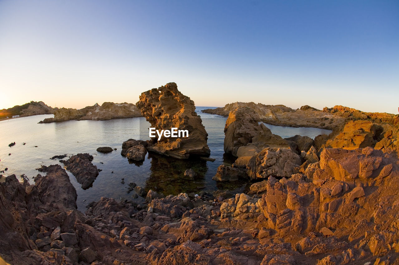 Rock formations on shore against clear sky