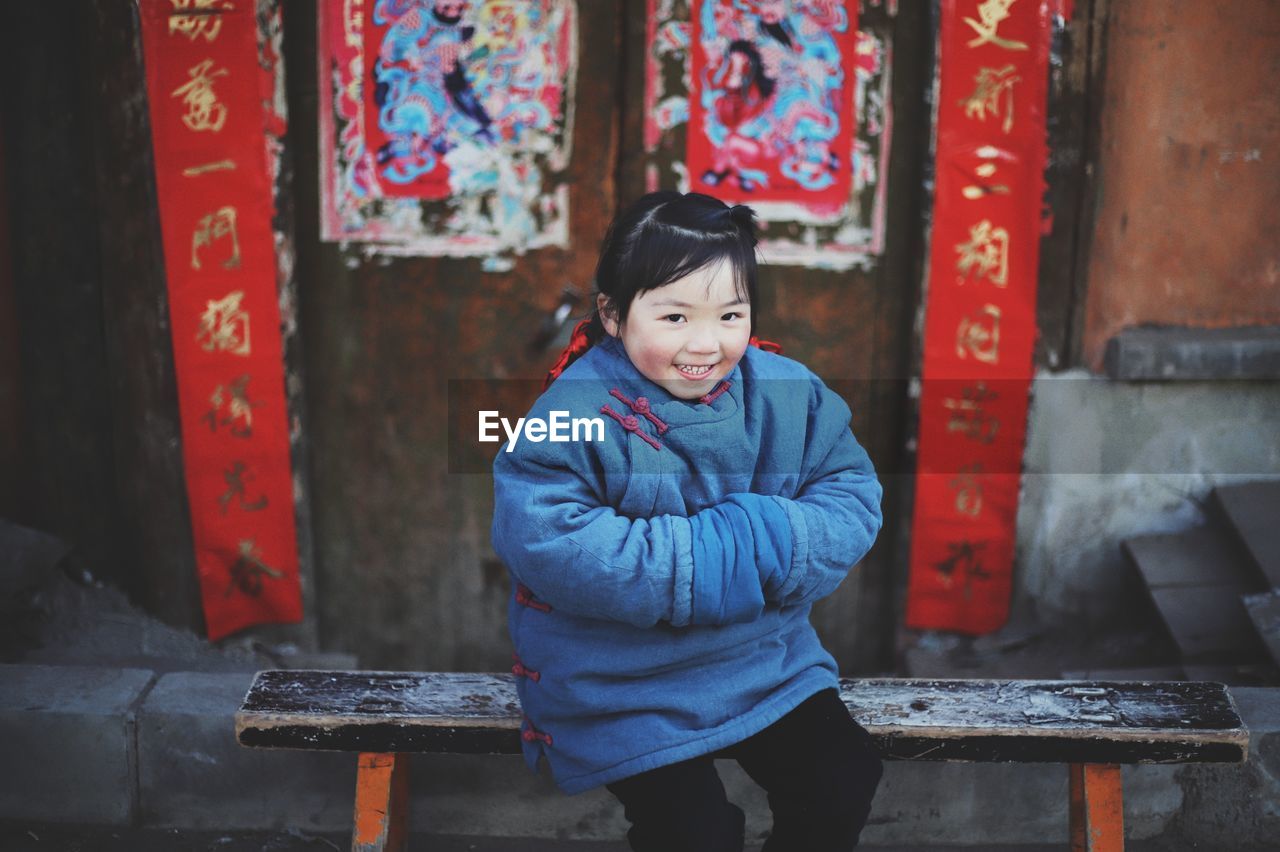 Portrait of smiling girl sitting on bench against wall