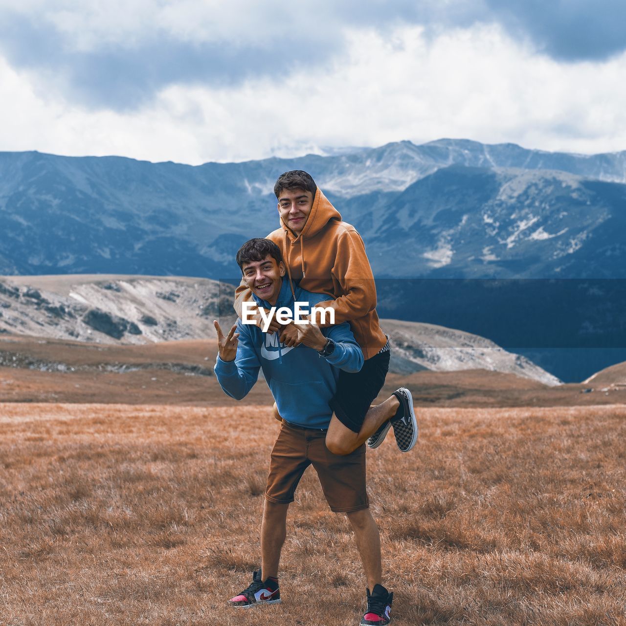 FULL LENGTH OF SMILING YOUNG MAN STANDING ON MOUNTAIN