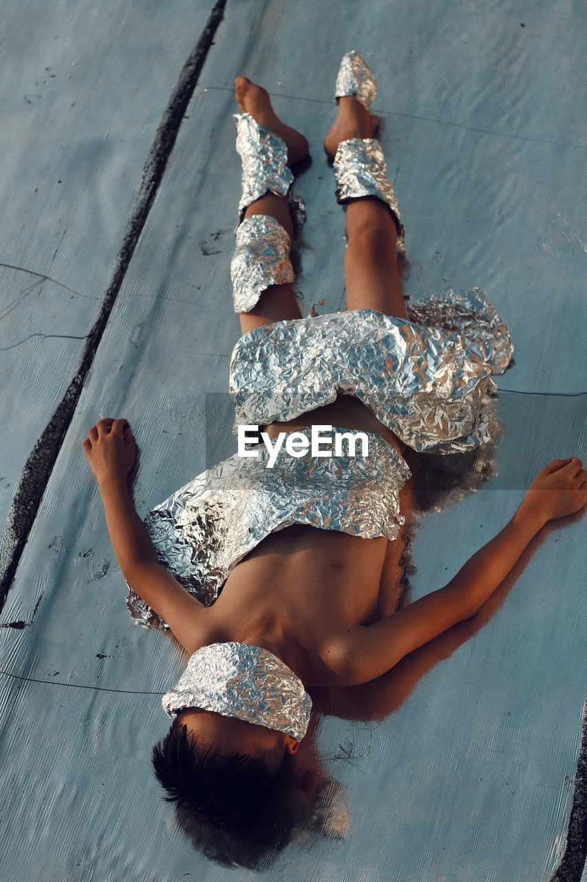 High angle view of naked boy covered with aluminum foils on field