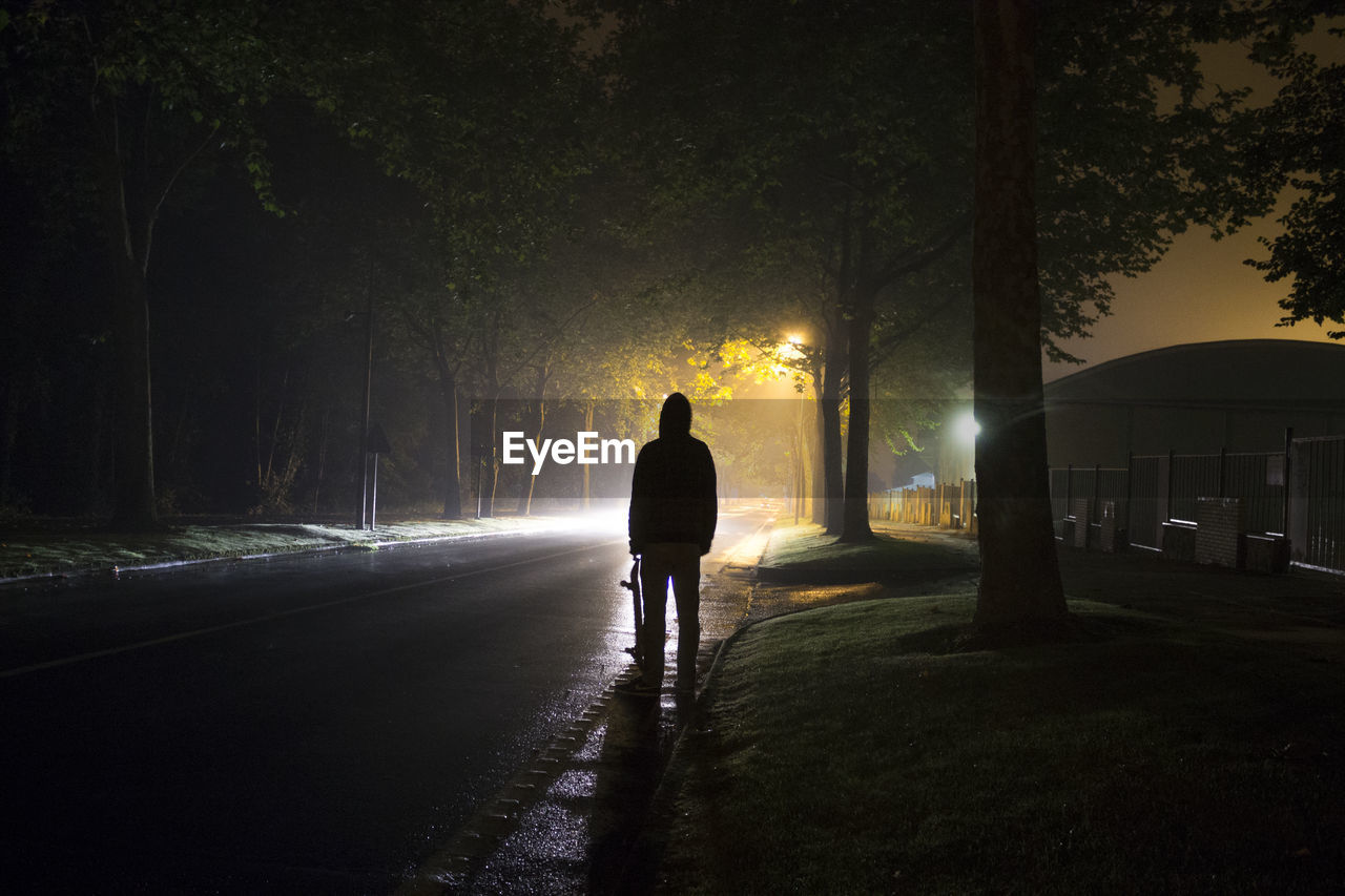 Rear view of skateboarder standing on road at night