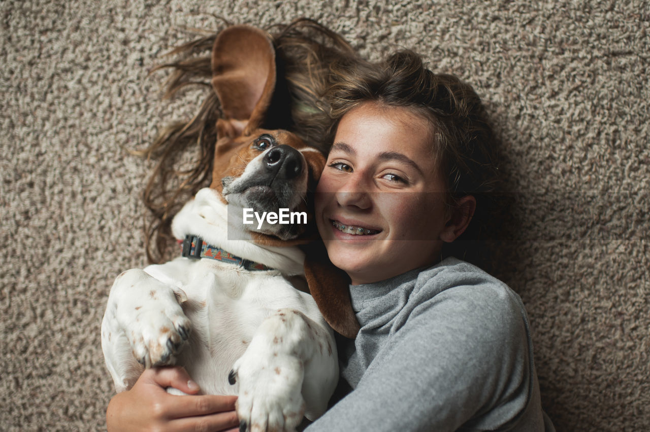 Tween girl posing with her basset hound dog while laying on the carpet