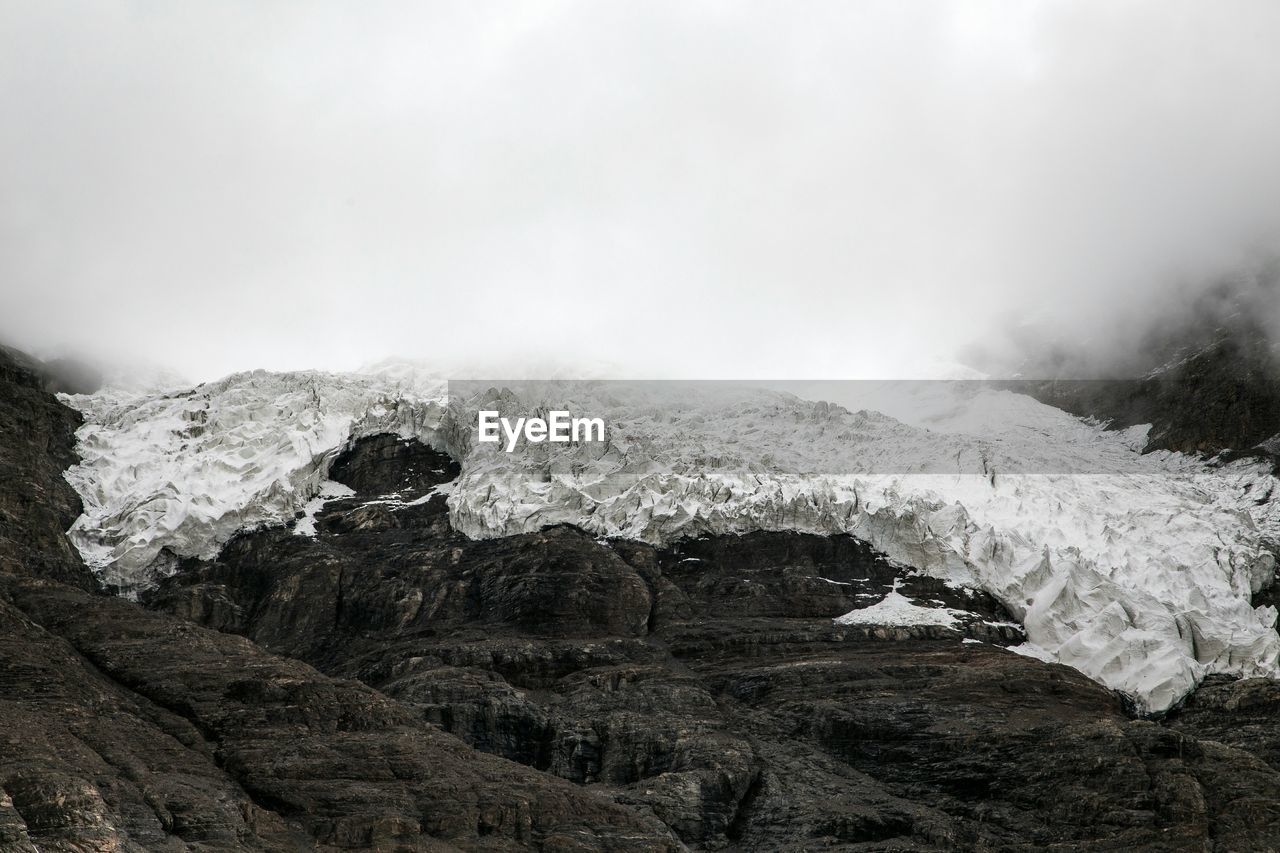 Low angle view of snow covered mountain during foggy weather