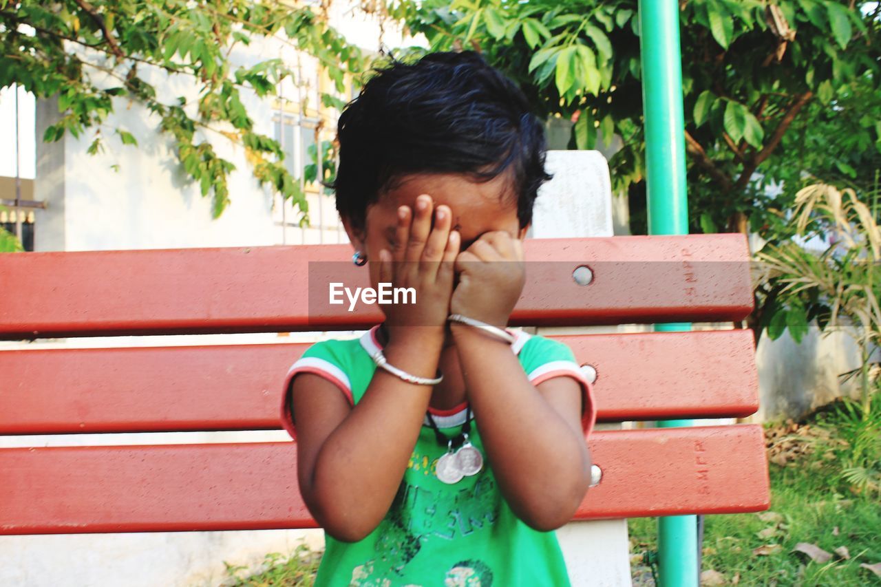 Girl with covering face while sitting on bench