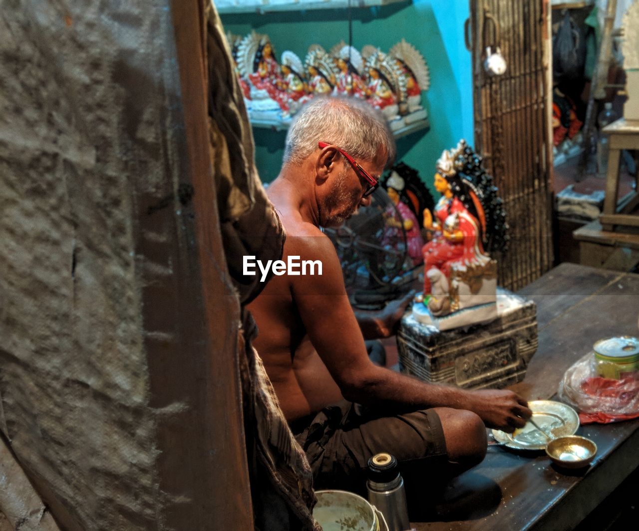 Shirtless man working on sculpture at workshop