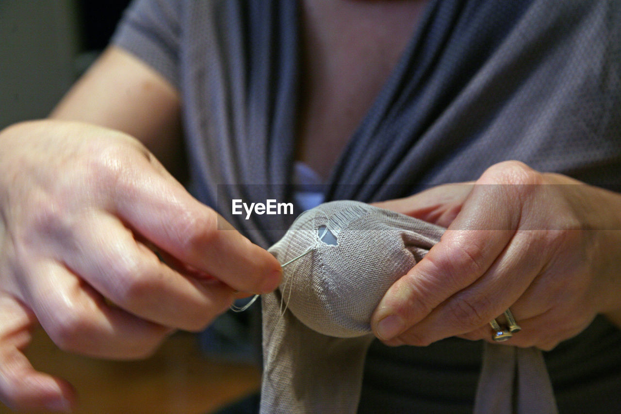 Midsection of woman stitching sock at home