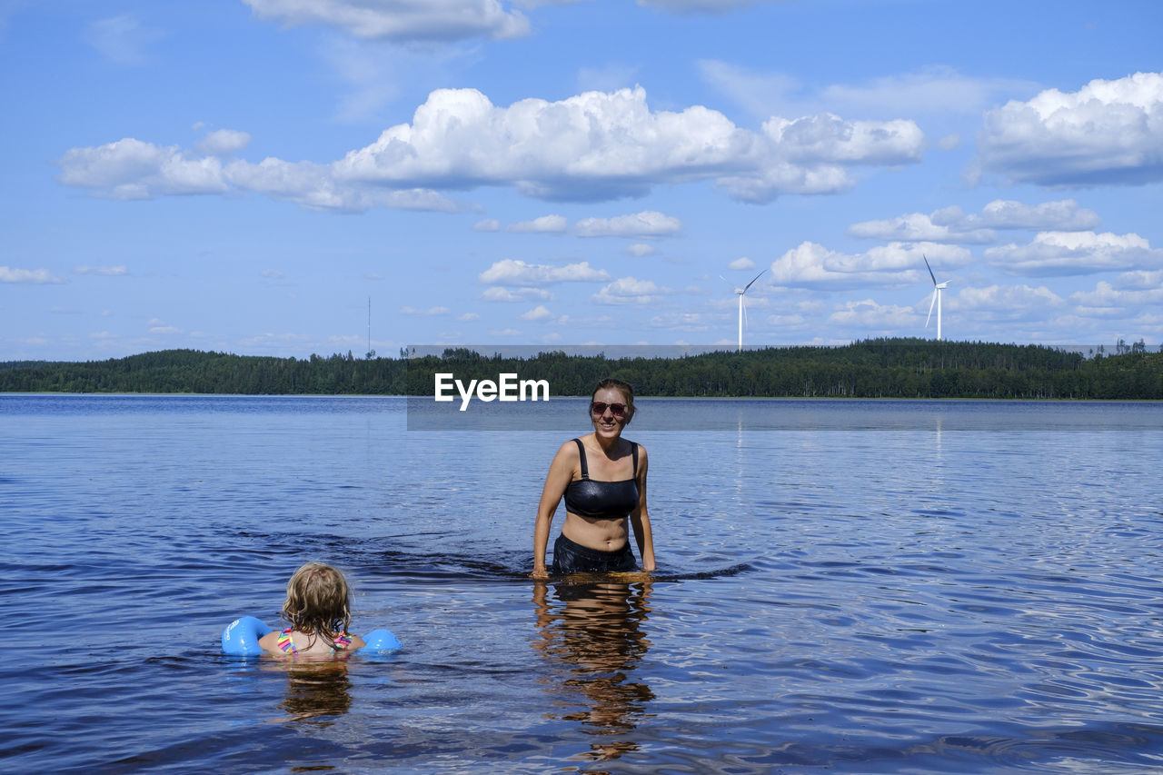 Portrait of woman and daughter in lake against sky