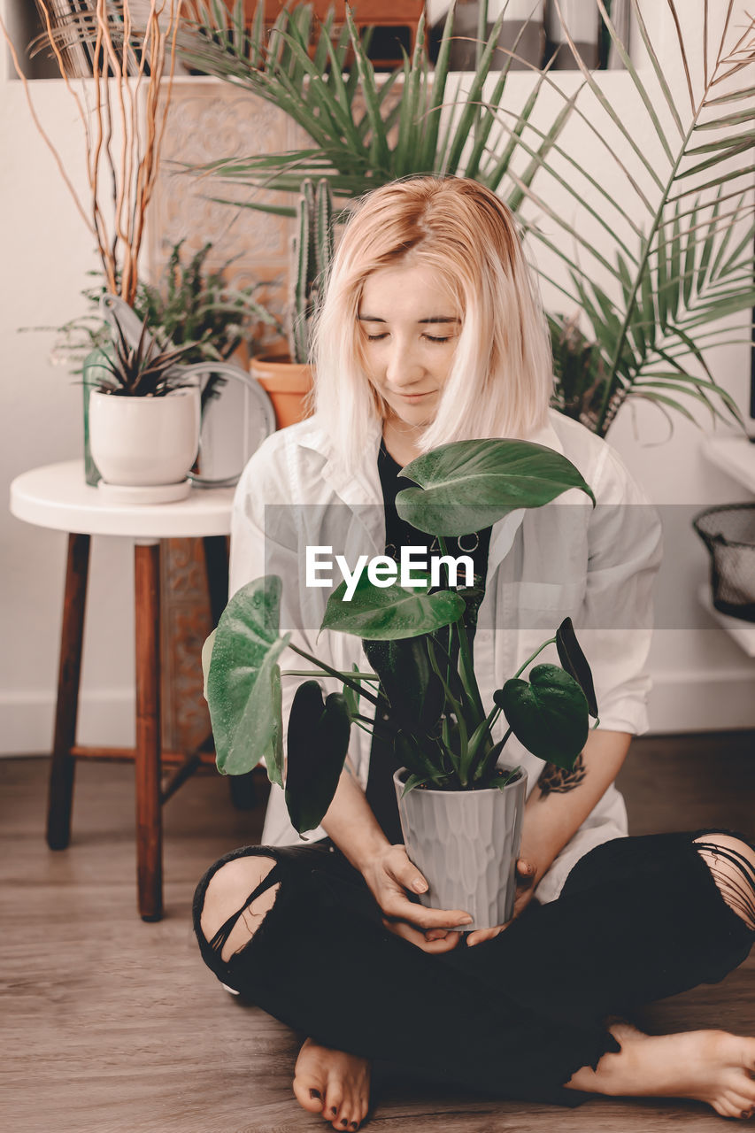 Young woman sitting on potted plant