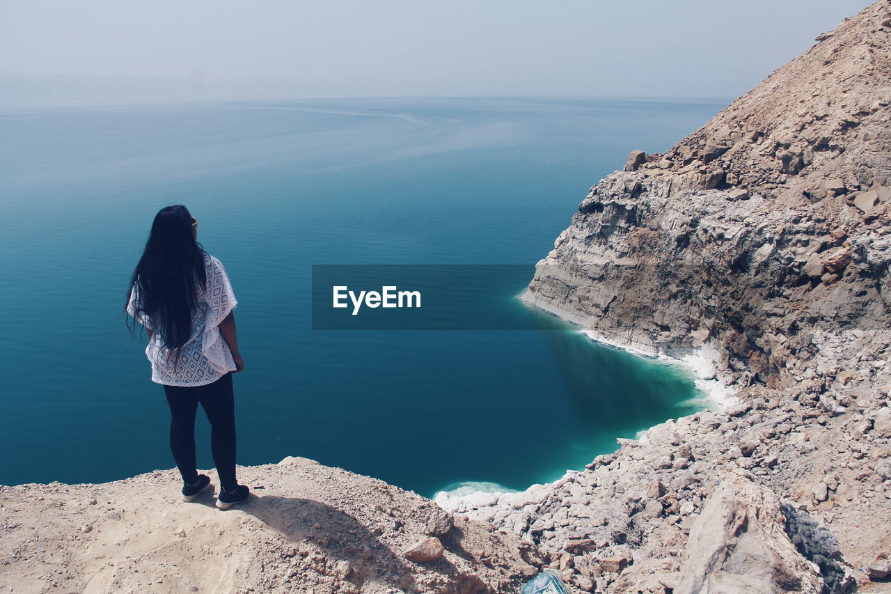 Rear view of girl standing on cliff by the sea