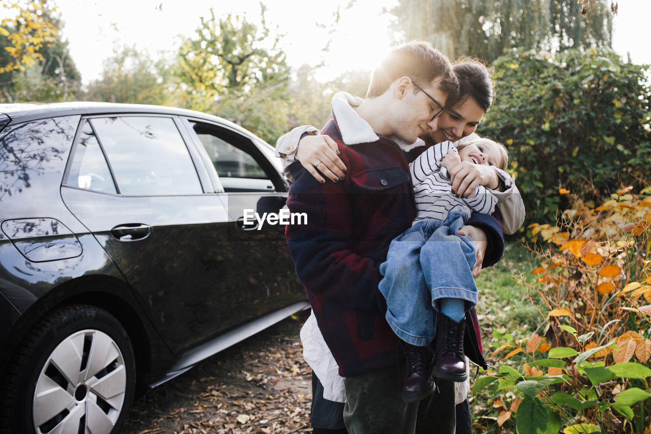 Father and mother playing with daughter near electric car during picnic