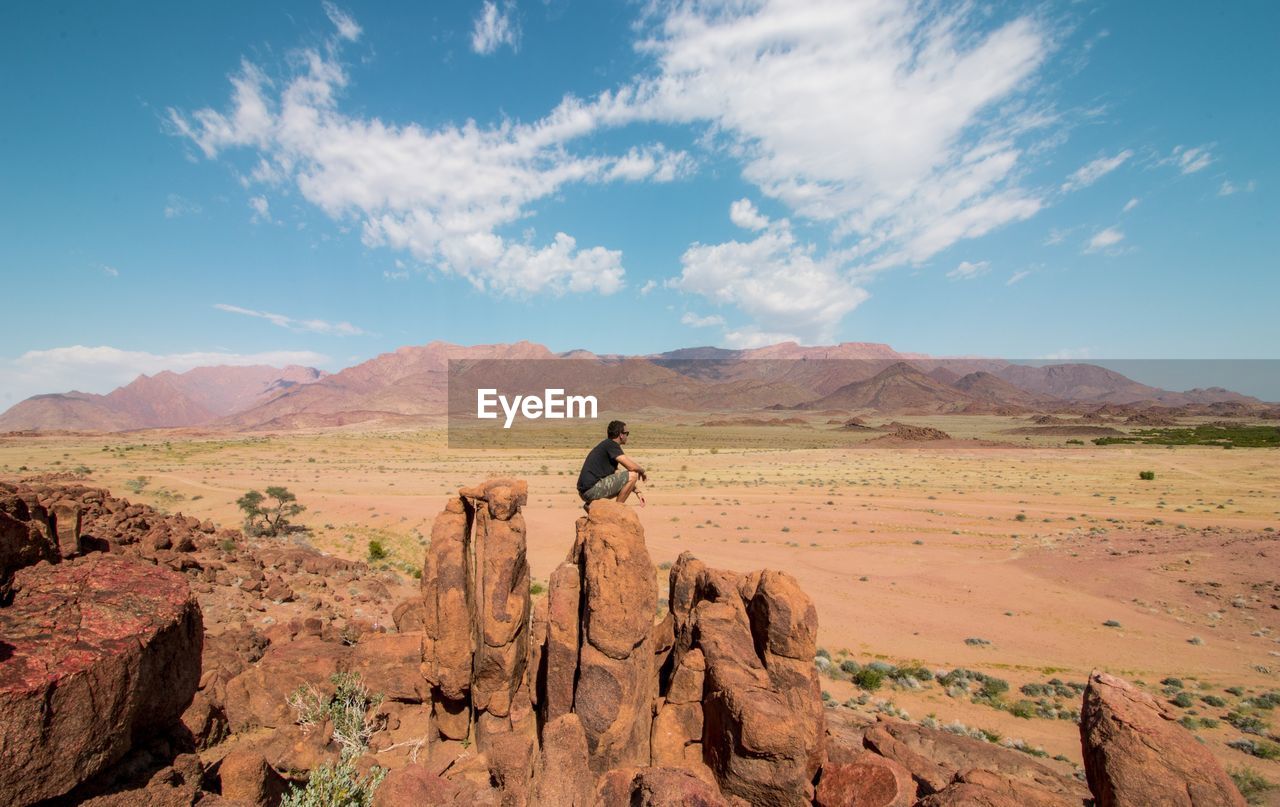 Side view of man sitting on rock in desert against sky
