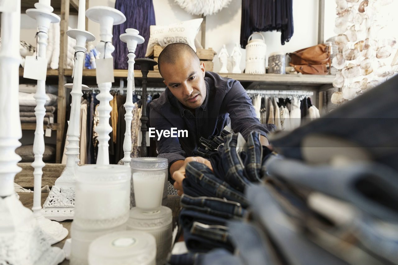 Male owner arranging jeans on table by candles at clothing store