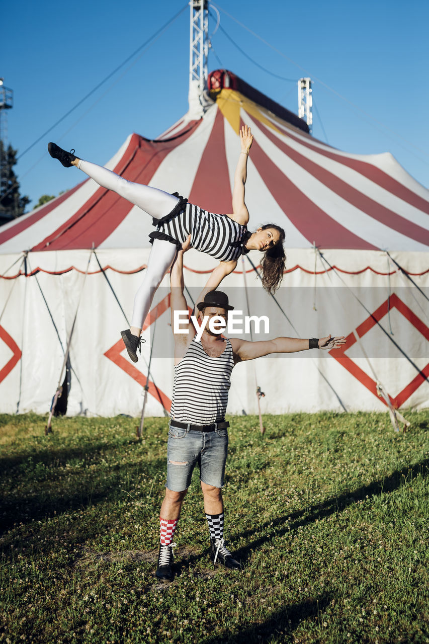 Muscular male acrobat lifting female performer while standing on meadow