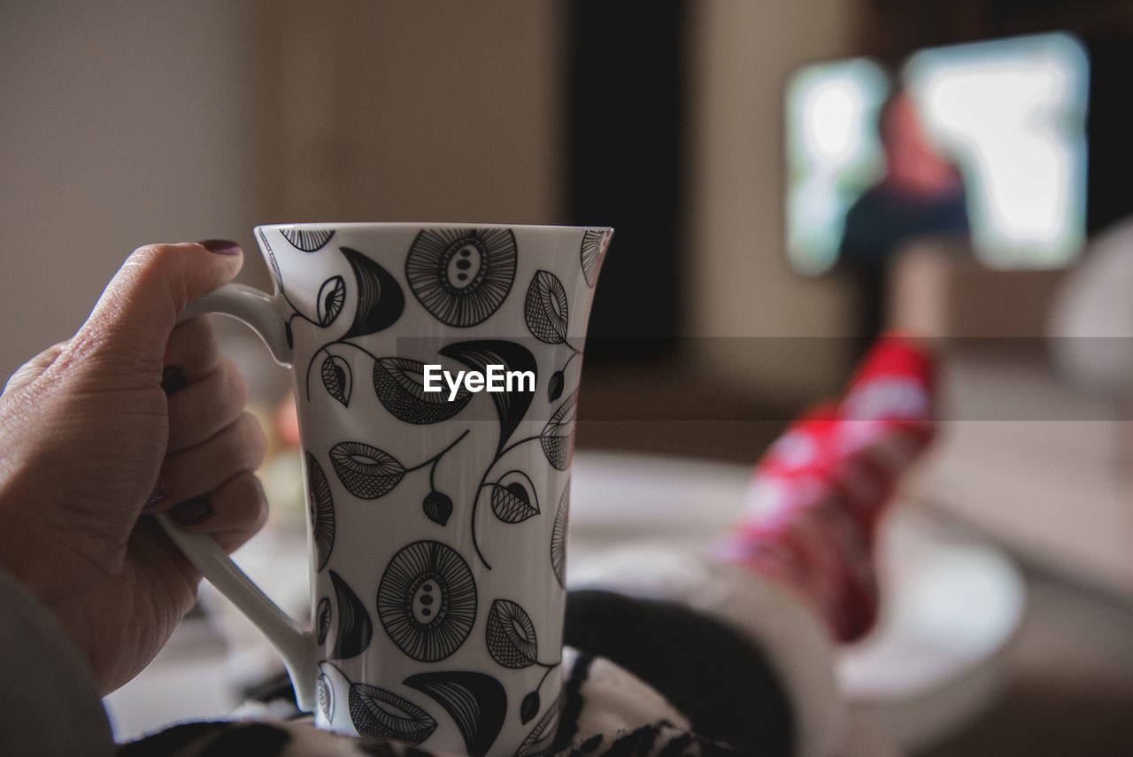 Low section of woman in warm clothing holding cup on table at home