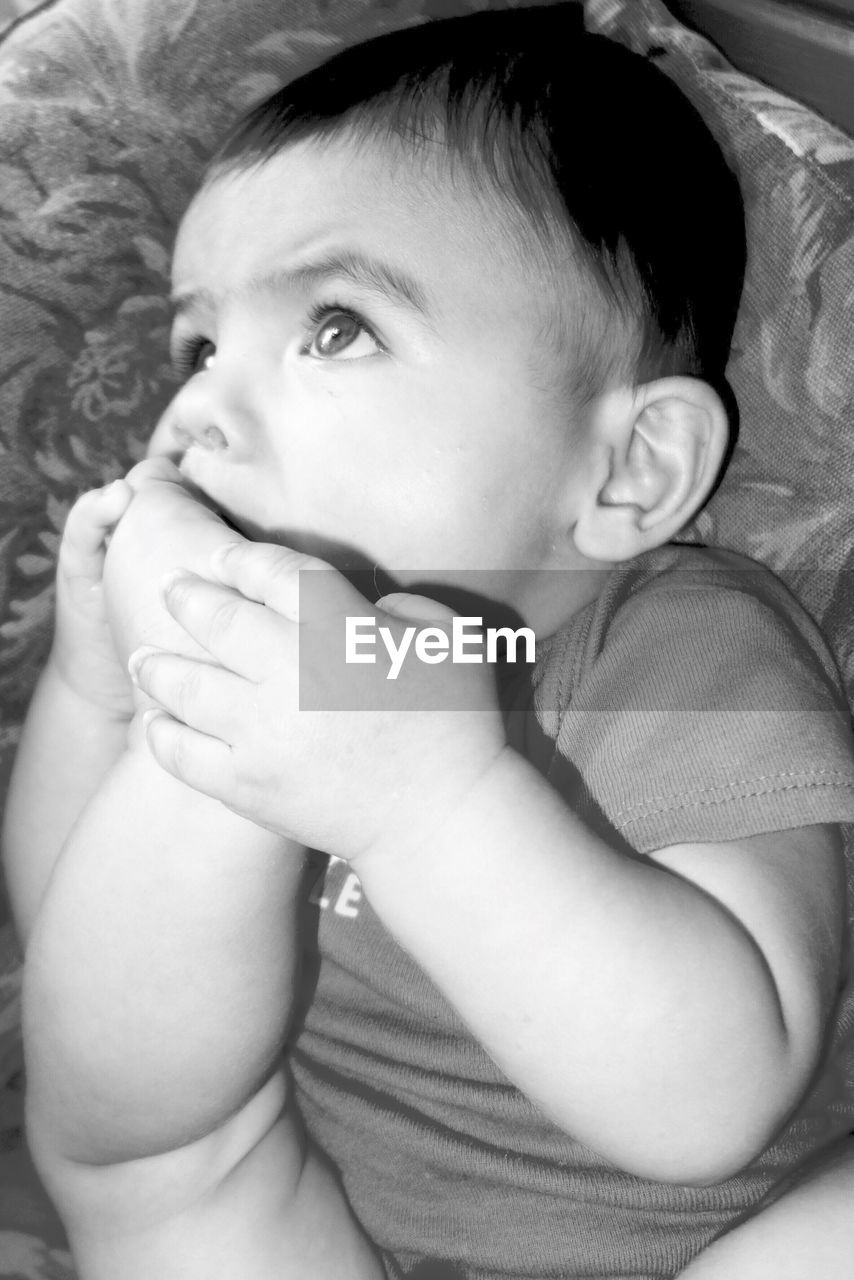 Baby boy biting feet while lying on bed