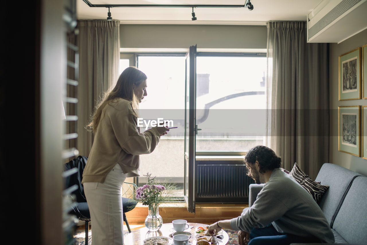 Couple in hotel room, woman taking photo of breakfast tray