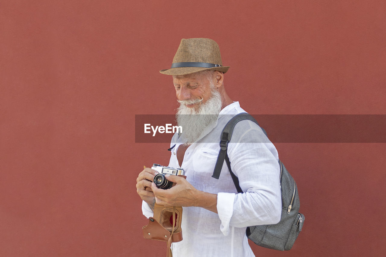 Smiling man holding camera while standing against wall