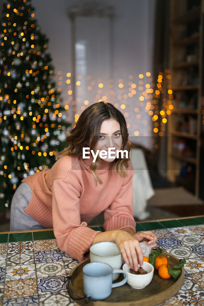 Portrait of smiling woman eating food against christmas tree