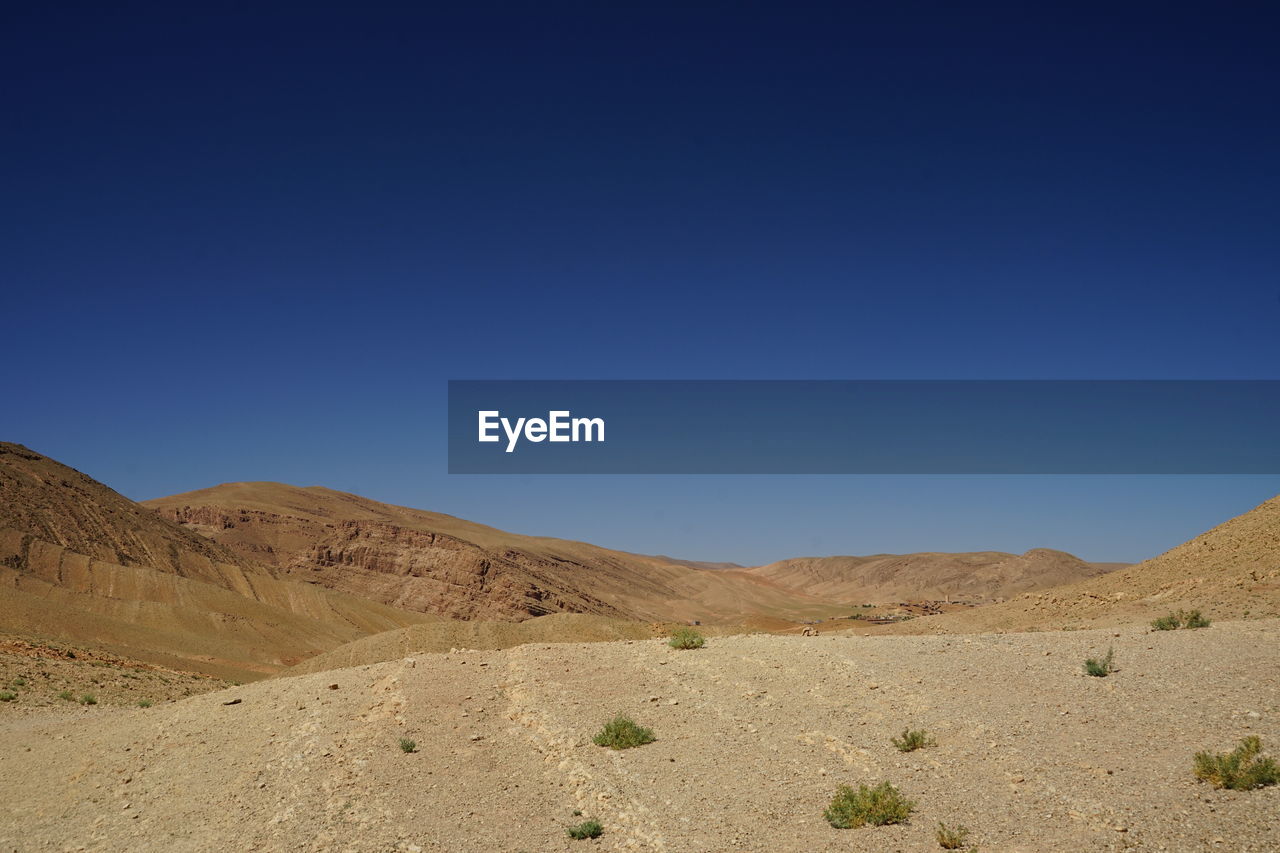 natural environment, landscape, environment, scenics - nature, desert, sky, land, climate, nature, blue, mountain, clear sky, sand, beauty in nature, arid climate, non-urban scene, wadi, no people, valley, tranquility, semi-arid, plateau, dry, sand dune, wilderness, travel, tranquil scene, mountain range, sunny, remote, travel destinations, sunlight, day, outdoors, extreme terrain, soil, erg, copy space, steppe, plain, tourism, grassland