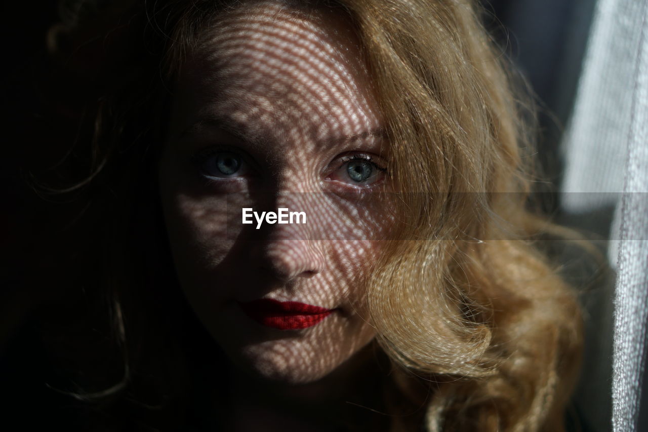 Close-up portrait of beautiful woman by curtain