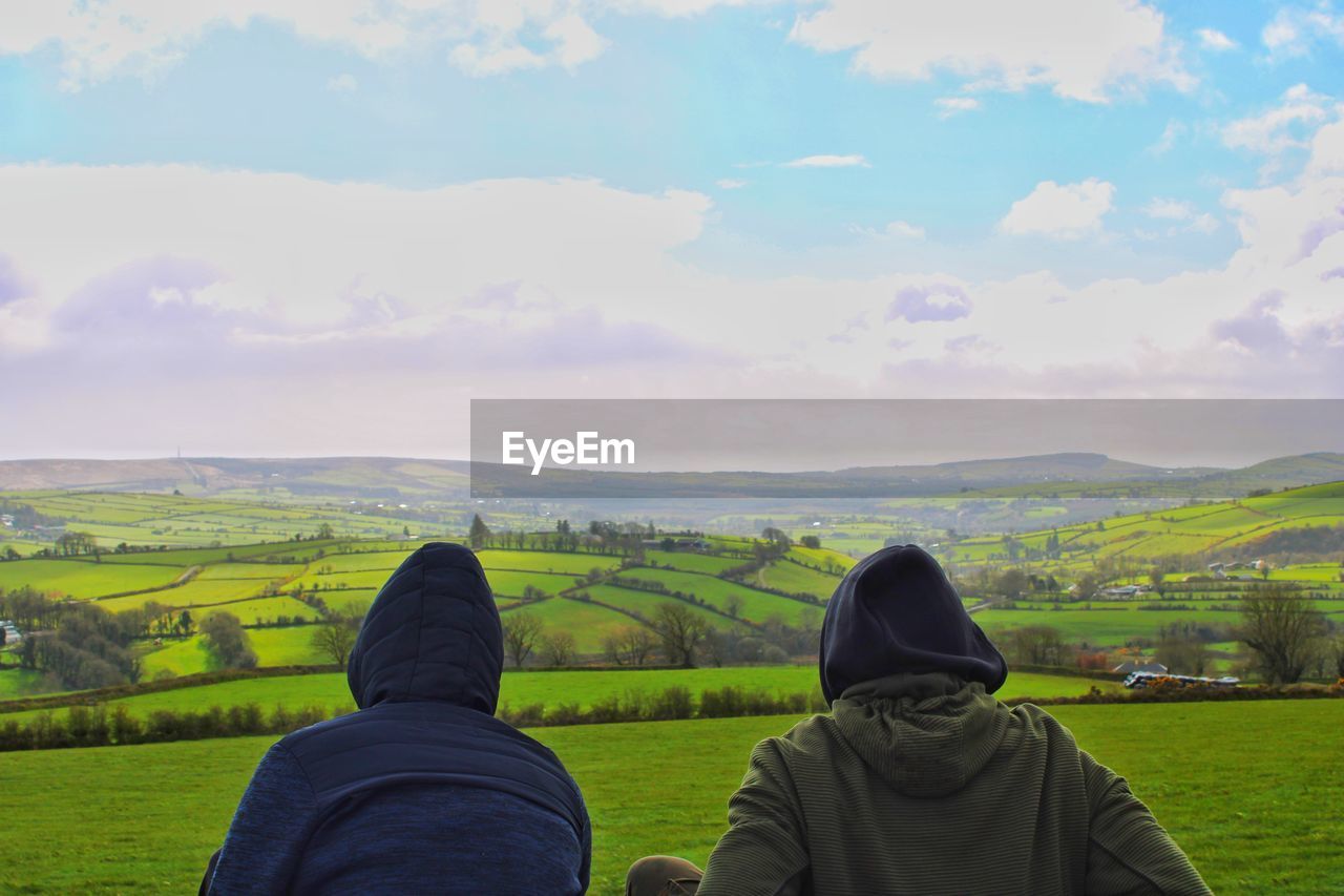 Rear view of people looking at field against sky