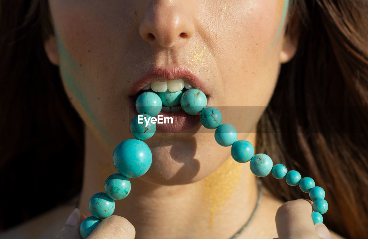 Close-up of woman carrying beaded necklace in mouth