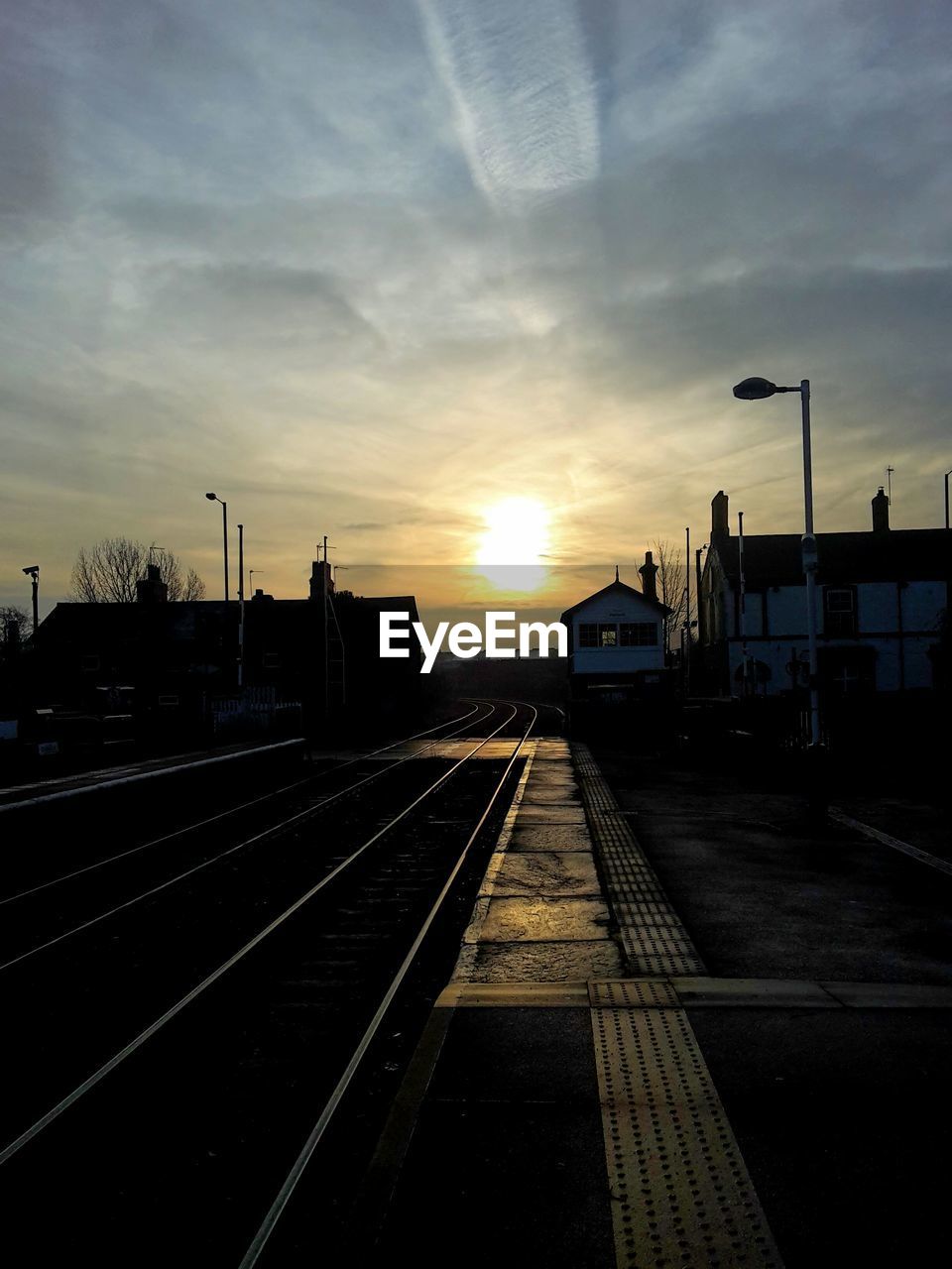 Railroad tracks by platform and buildings against cloudy sky during sunset