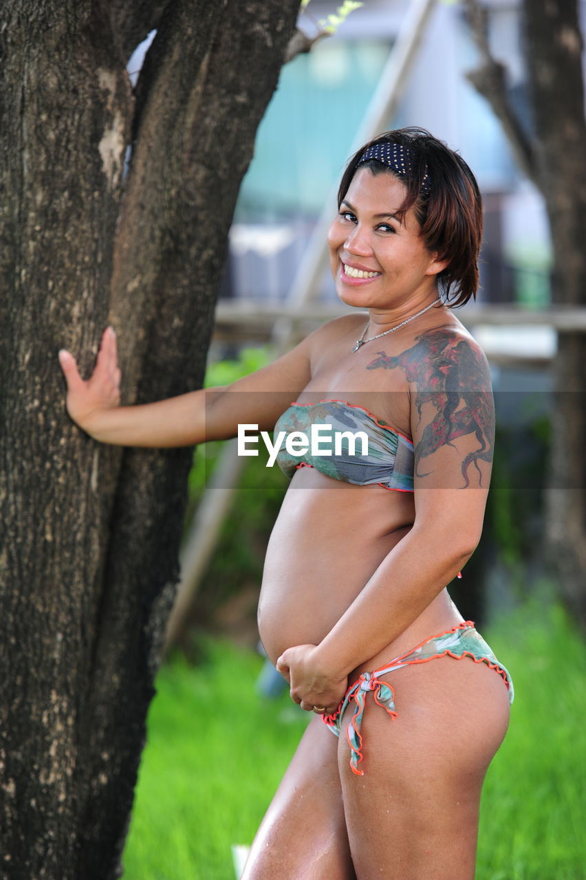 Portrait of pregnant woman standing by tree trunk