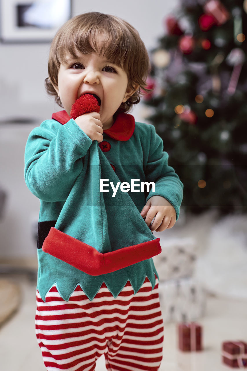 A little 12-month-old christmas elf with a christmas tree and gifts