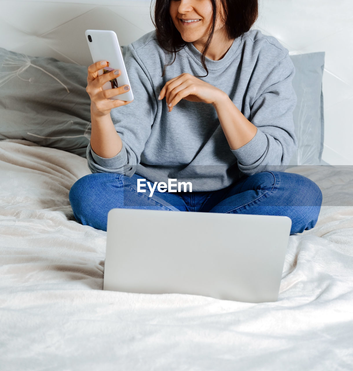 Midsection of woman using smart phone while sitting on bed