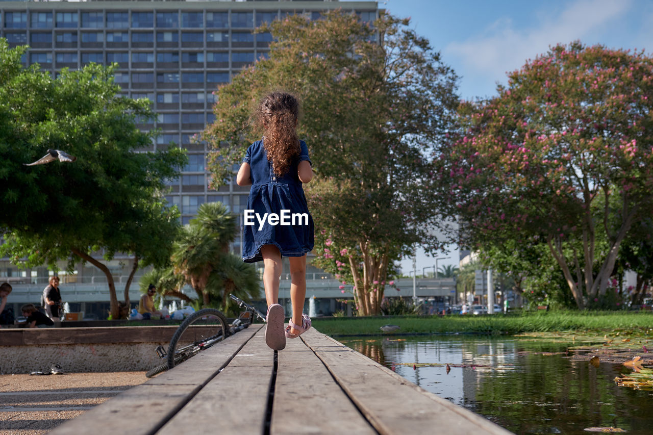 Rear view of girl running on footbridge over lake