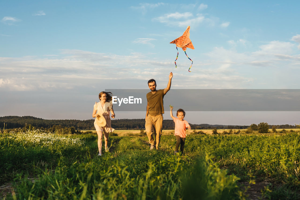 Family running on grassy land against sky