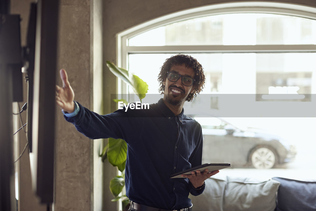 Happy businessman with digital tablet gesturing at creative office