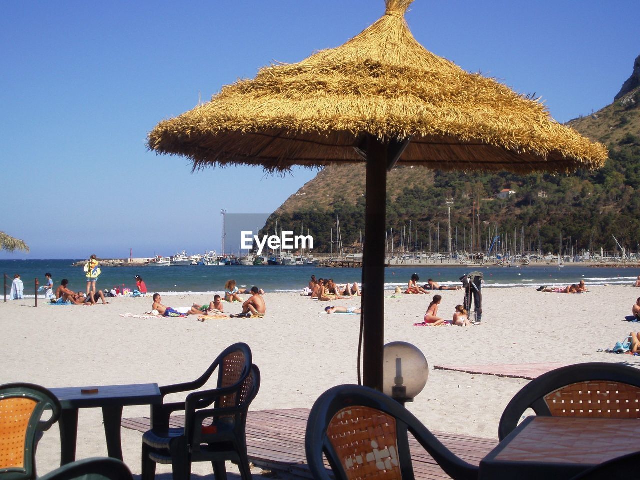 Thatched roof and chairs against people relaxing at beach