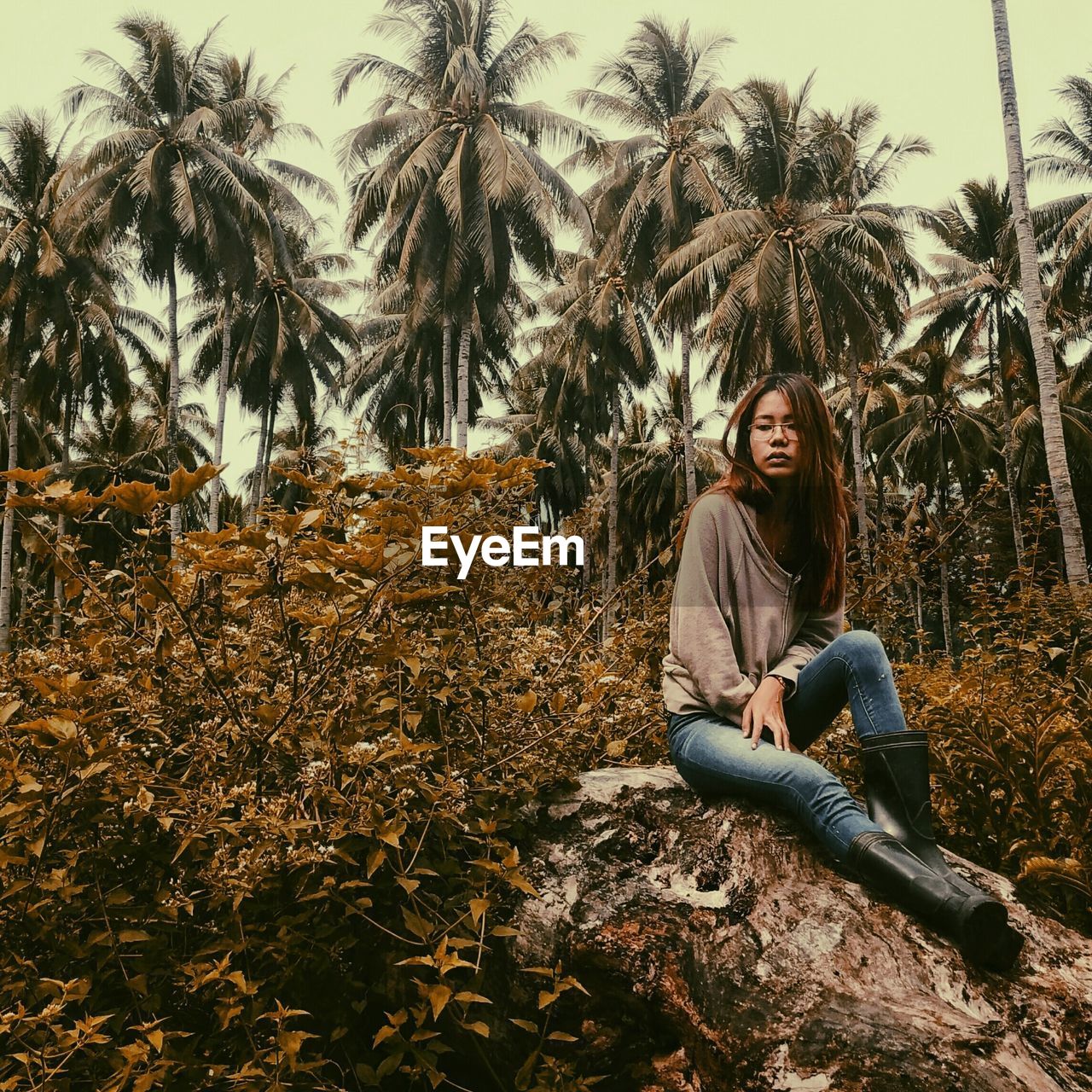 Young woman looking away while sitting on rock