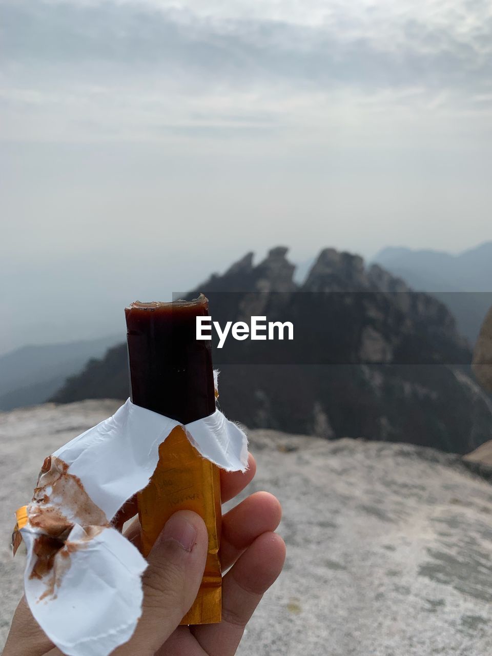PERSON HOLDING ICE CREAM AGAINST MOUNTAIN
