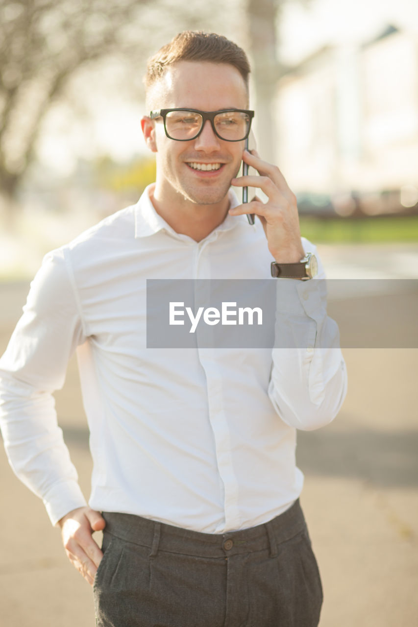 Smiling young man talking on mobile phone while standing in city