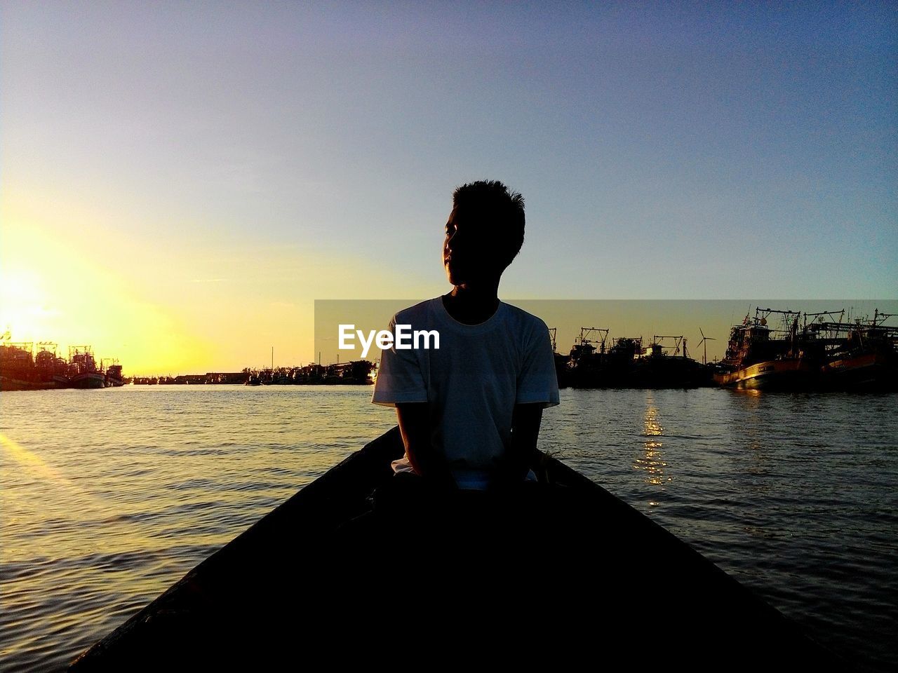 Young man sitting in boat on sea against sky during sunset