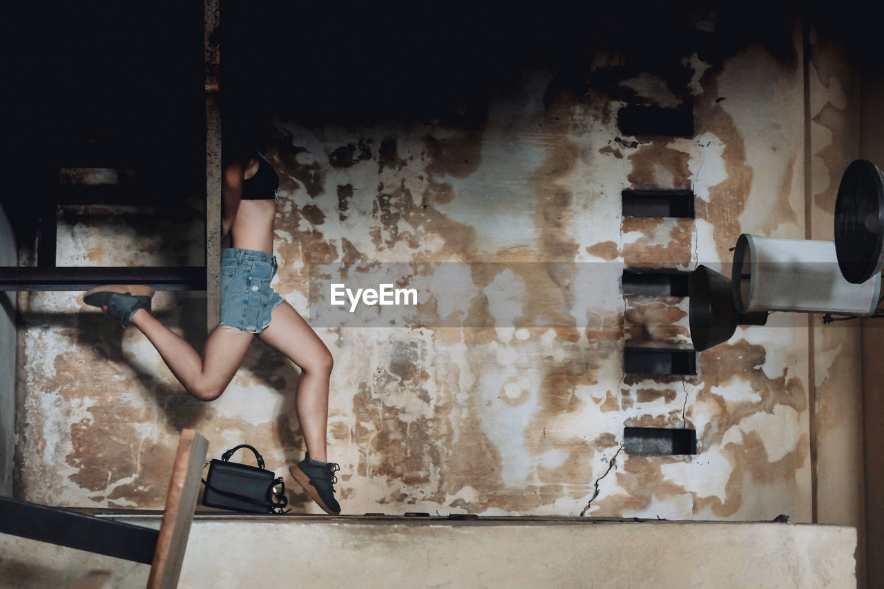 SIDE VIEW OF WOMAN STANDING AGAINST WALL IN ABANDONED BUILDING