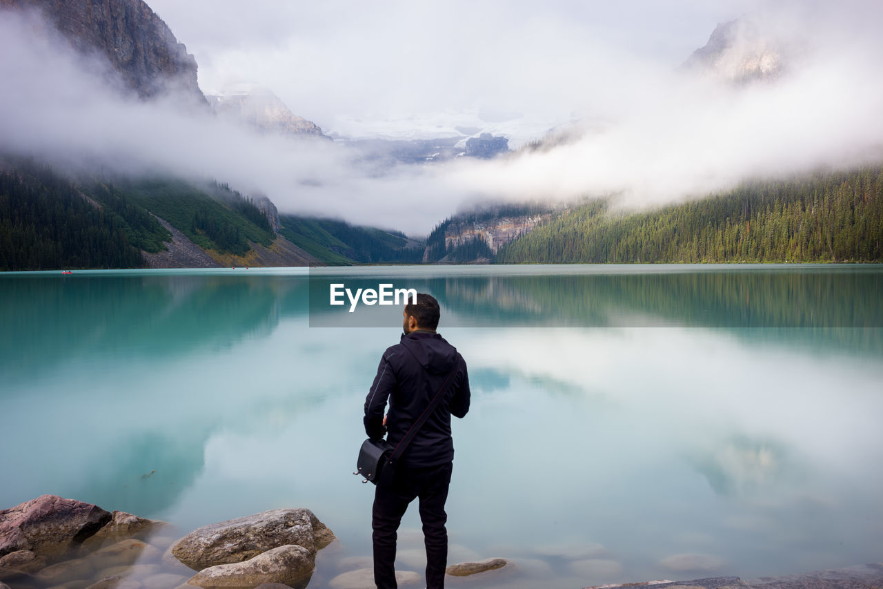 Rear view of man looking at lake against mountain