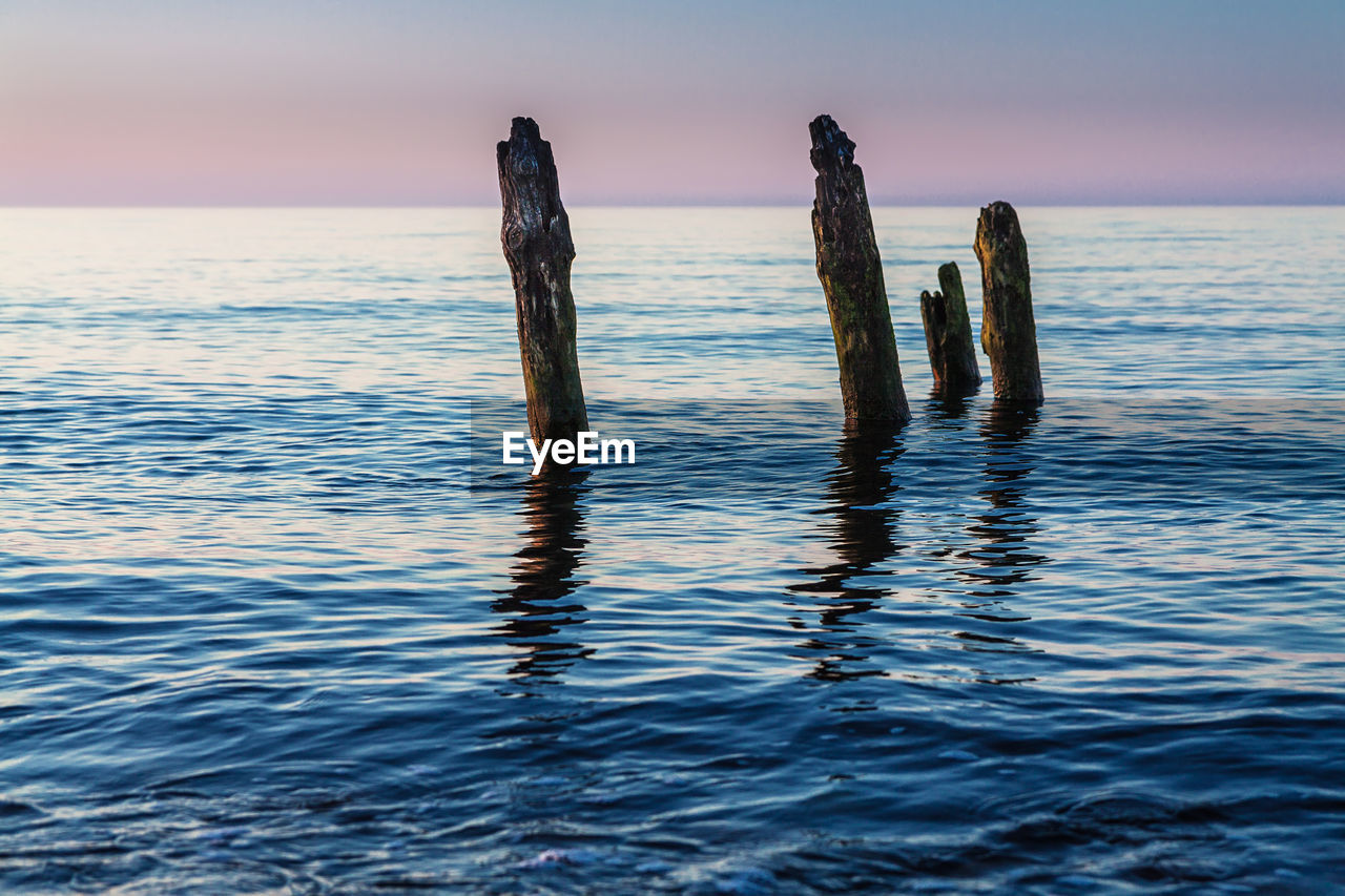 Weathered wooden posts in sea during sunset