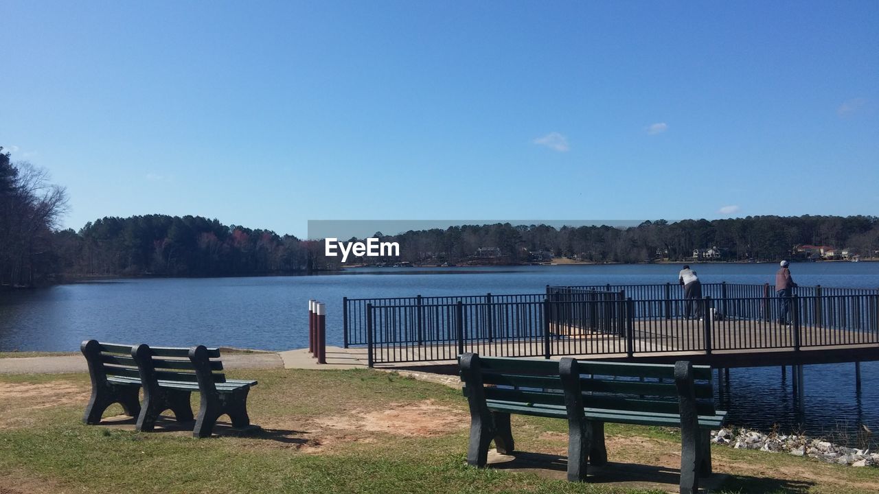 EMPTY BENCH ON LAKE AGAINST BLUE SKY