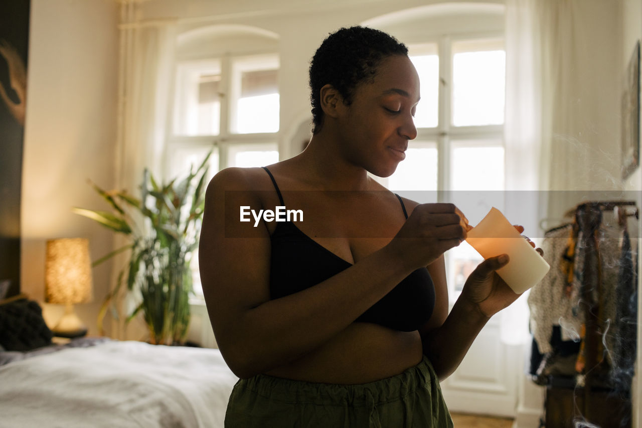 Smiling young woman holding lit candle in bedroom at home