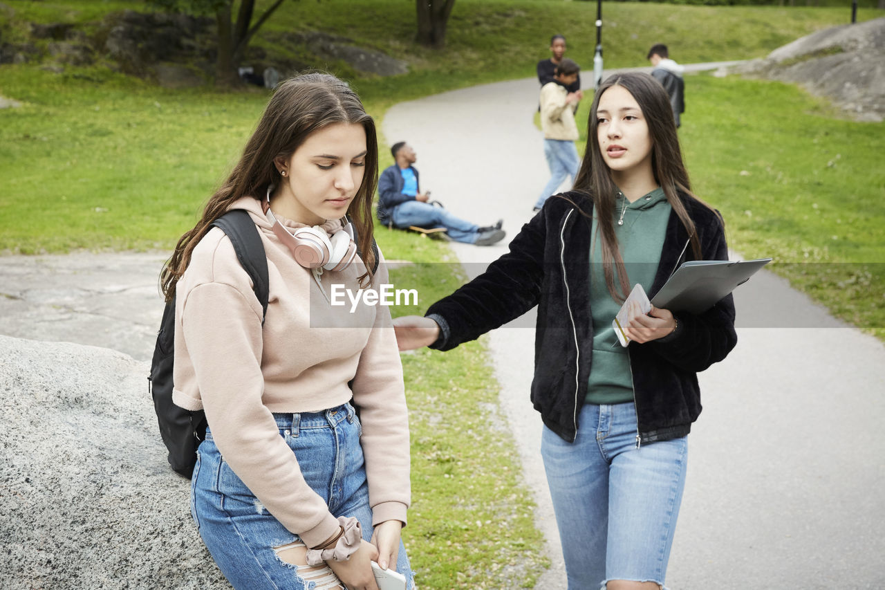 Teenage girl consoling sad female friends sitting on rock at park