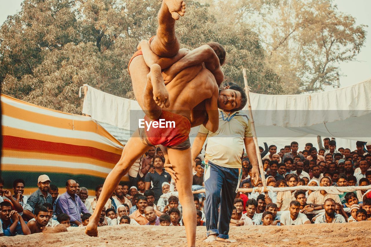 REAR VIEW OF SHIRTLESS MAN STANDING BY TREE