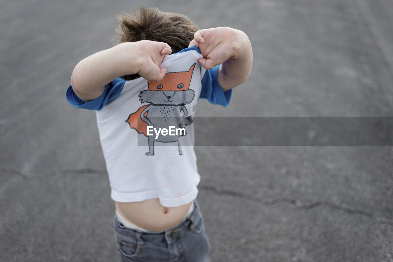 High angle view of boy removing t-shirt while standing on footpath