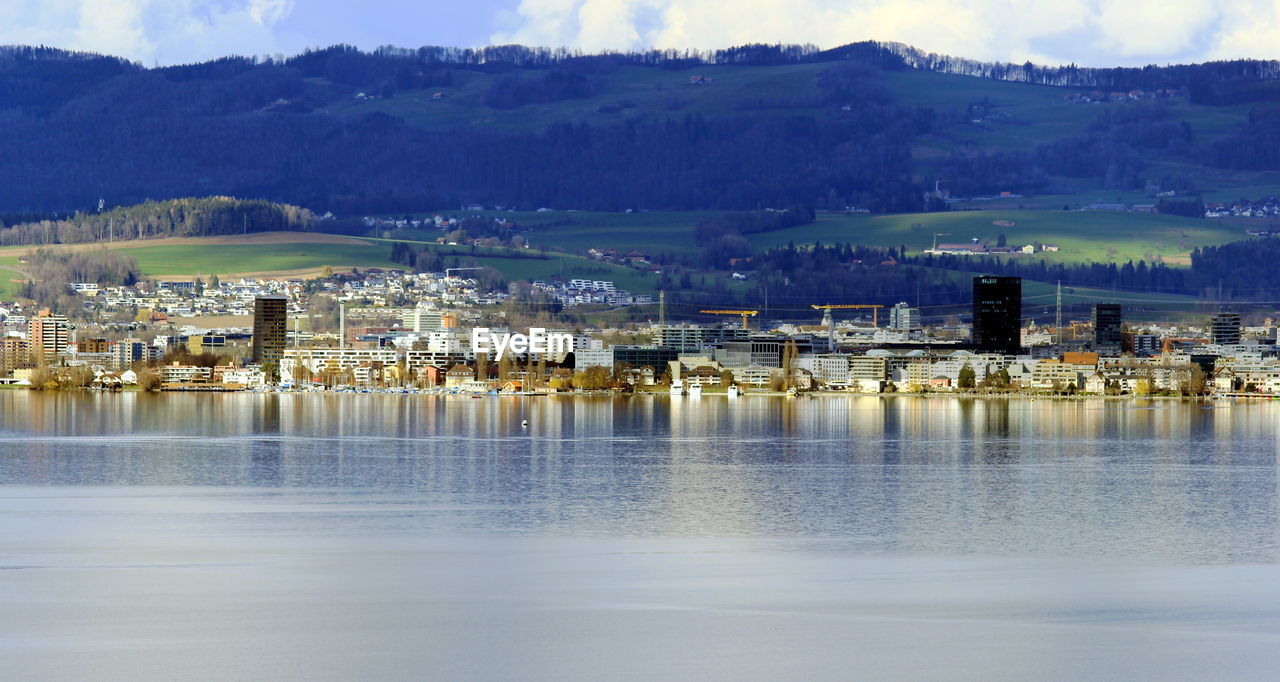 SCENIC VIEW OF LAKE BY BUILDINGS AGAINST MOUNTAIN