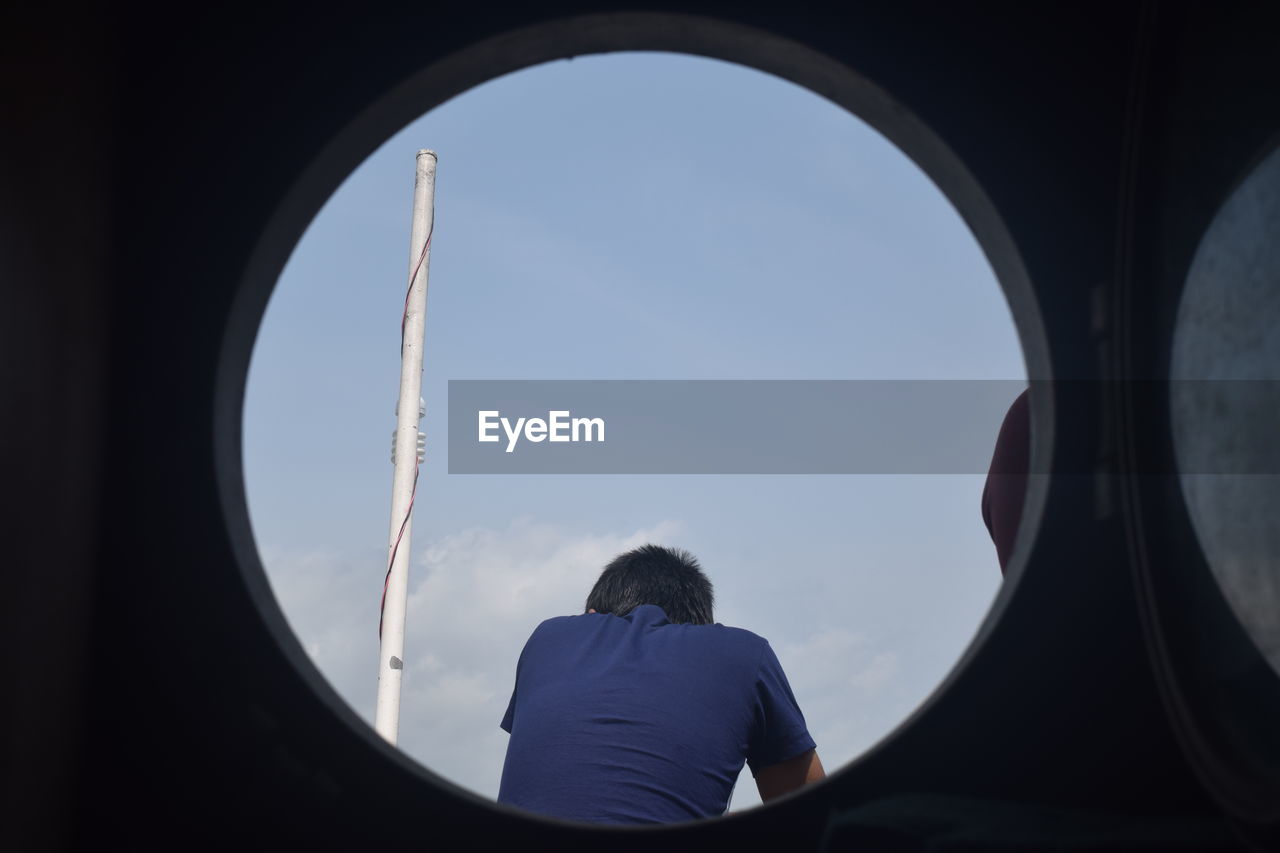 REAR VIEW OF MAN LOOKING THROUGH AIRPLANE WINDOW