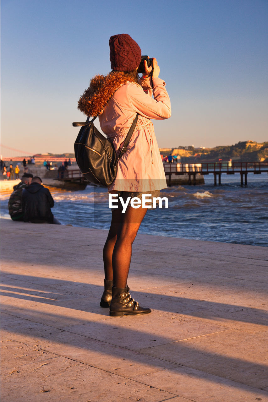 WOMAN STANDING AT BEACH AGAINST SKY