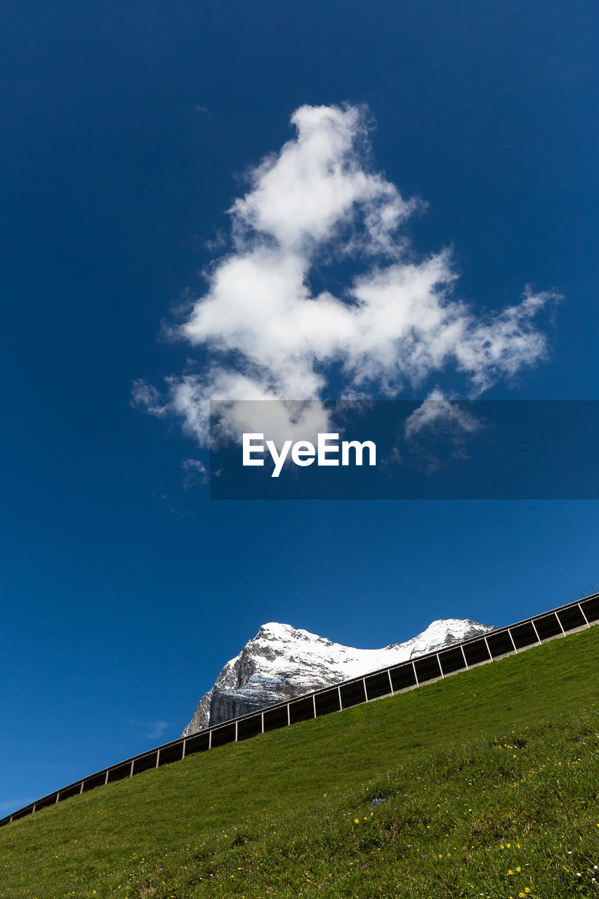 Tilt image of hill and snowcapped mountain against sky